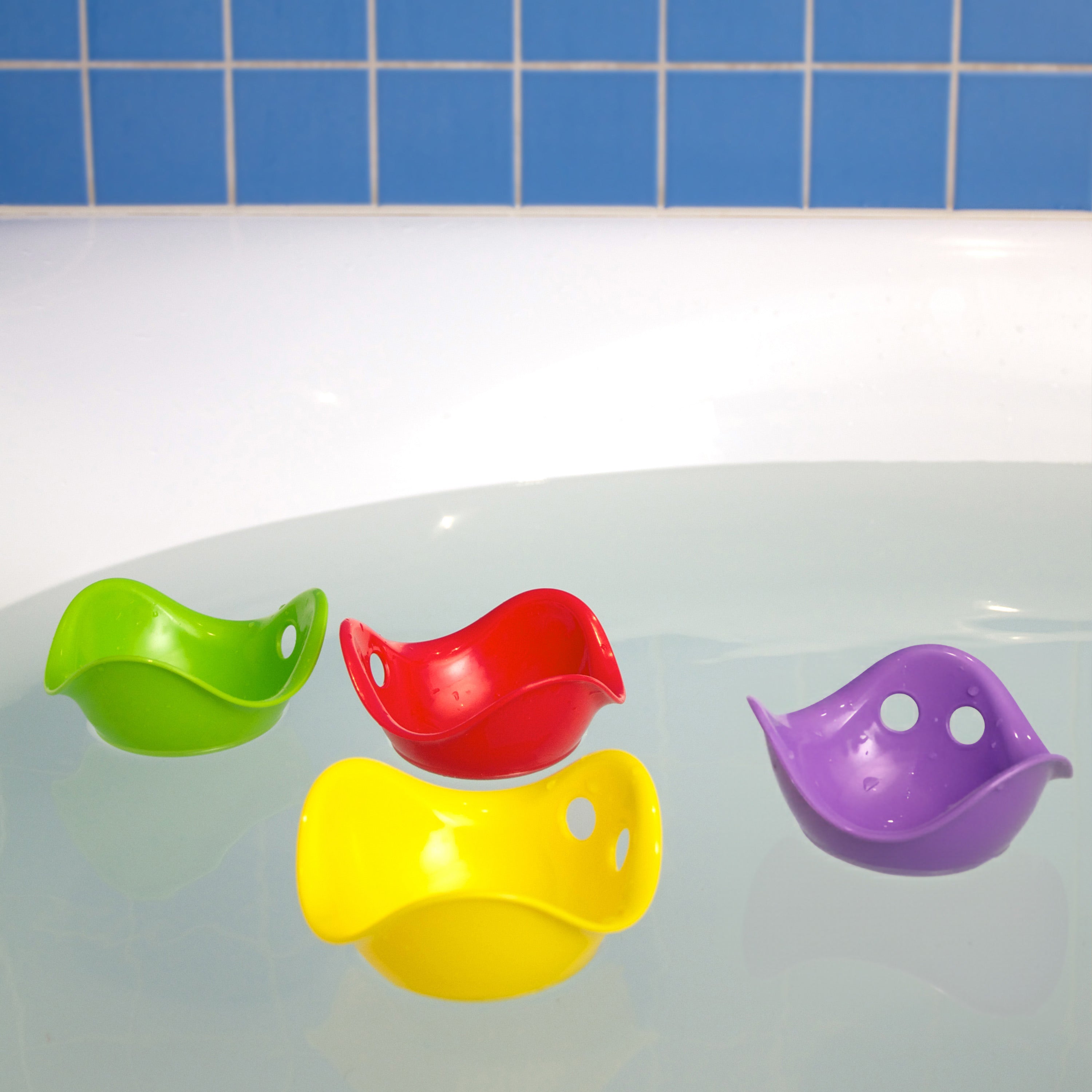 Four colorful Bilibo Mini sensory play shells by MOLUK floating in the bathtub.