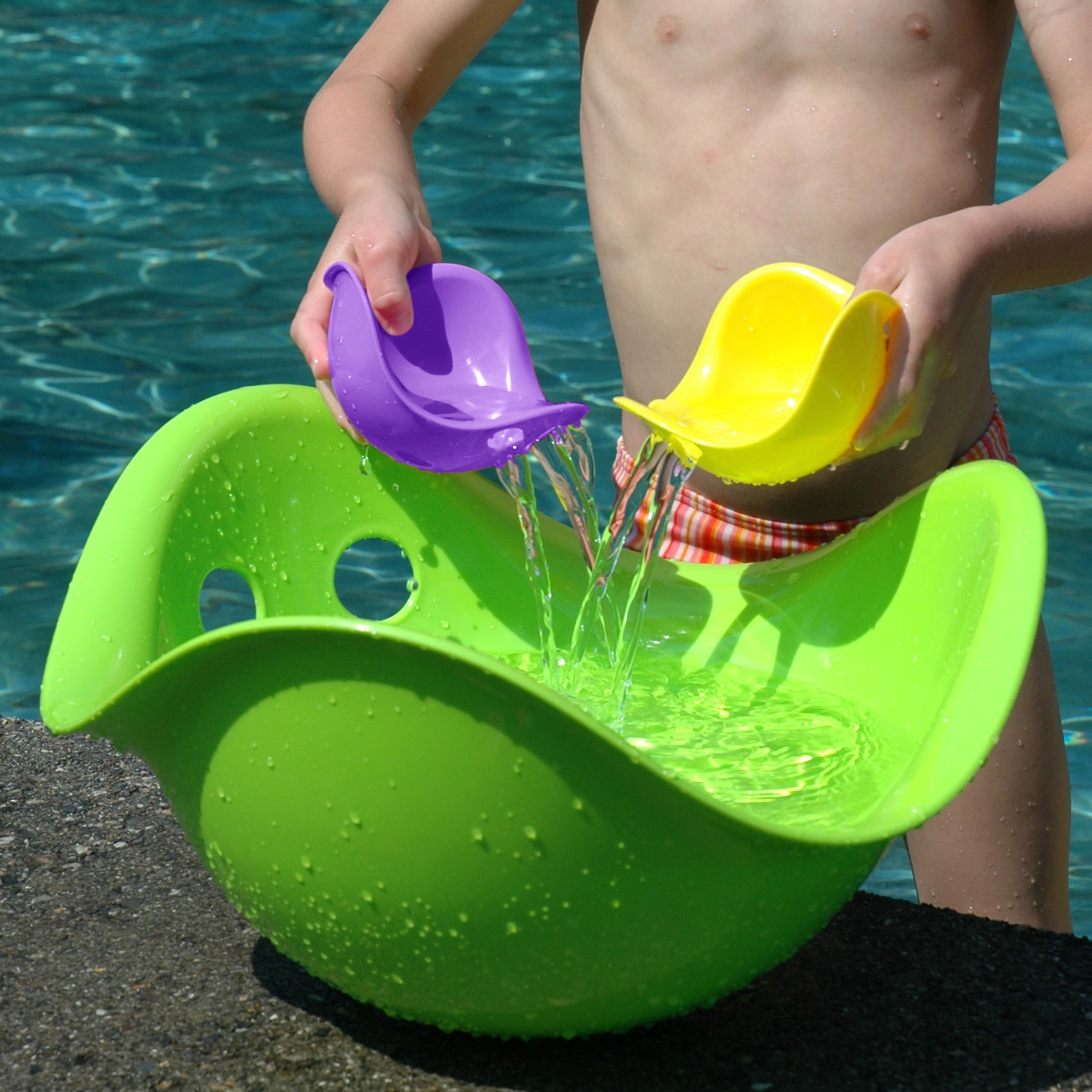 Child pouring water into a large green Bilibo with two Bilibo Mini play shells by MOLUK.