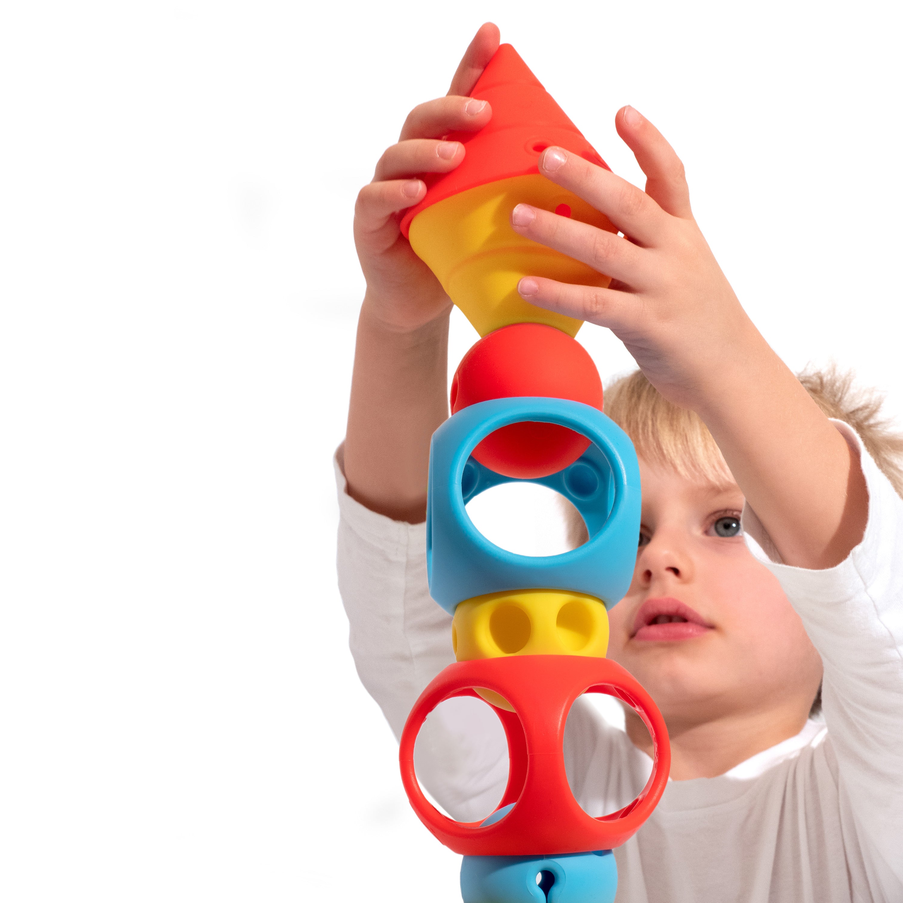 Boy building a tall tower with the BUILDING GENIUS set by MOLUK, stacking silicone Hix cones, Mox balls, and Oibo blocks in bright primary colors.
