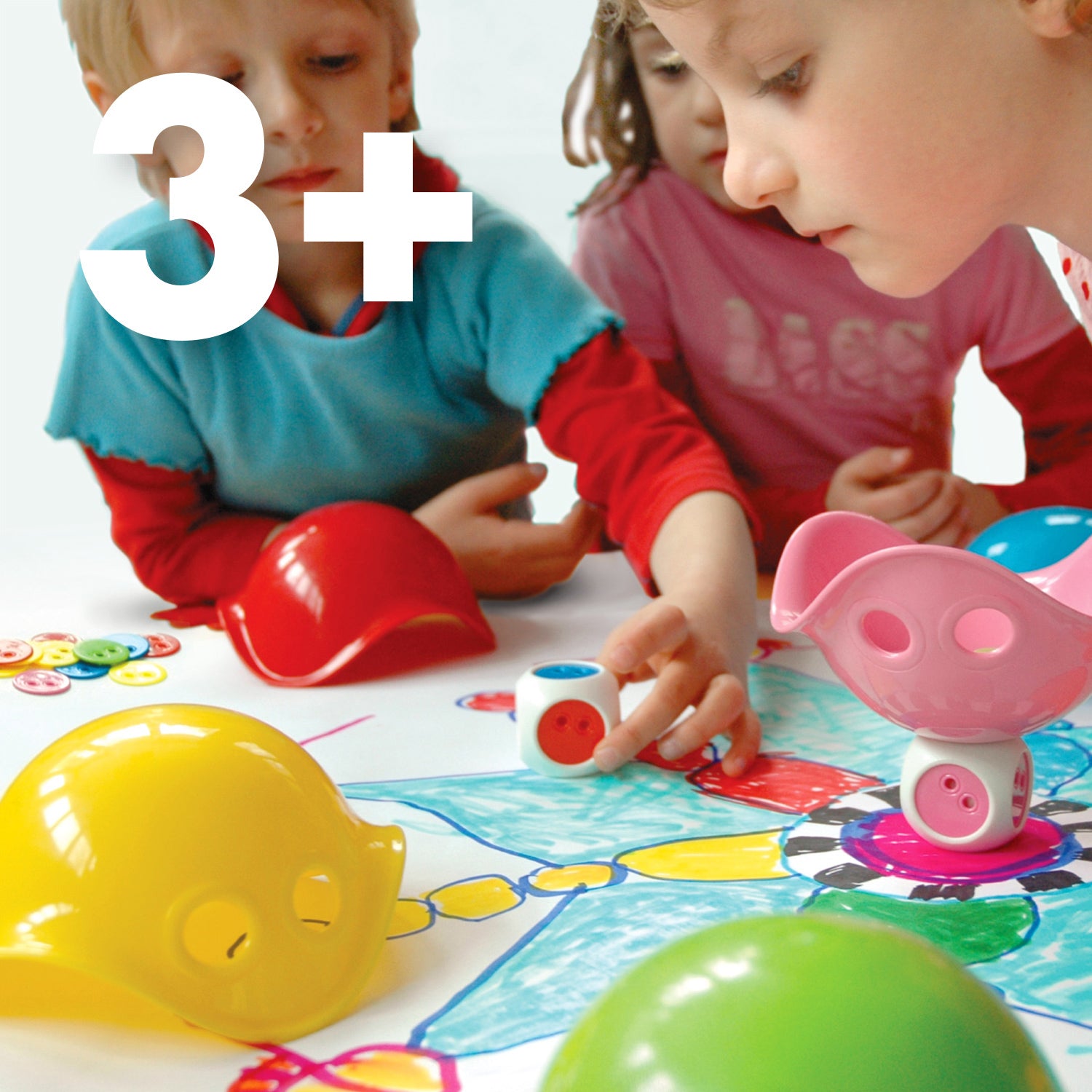 Three children playing with educational Bilibo Game Box set by MOLUK including a dice and color chips, a '3+' age recommendation shown.