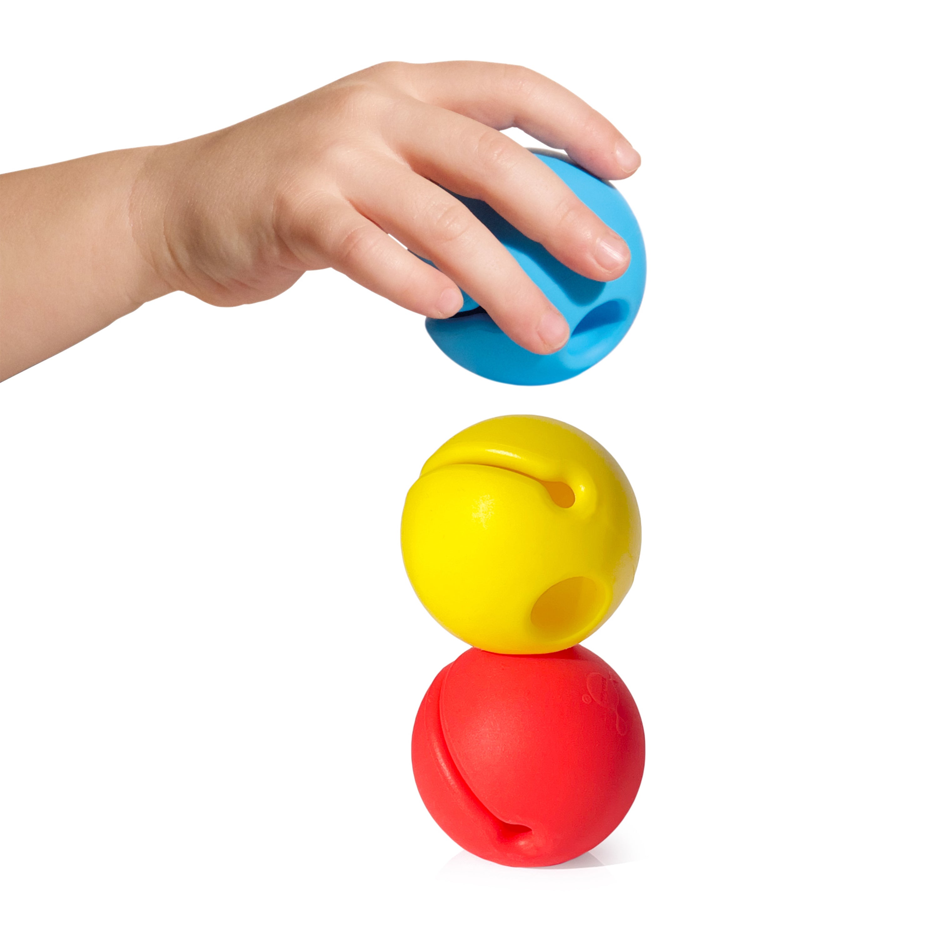 Child’s hand stacking colorful Mox silicone balls by MOLUK in blue, yellow, and red, exploring balance and playful construction.