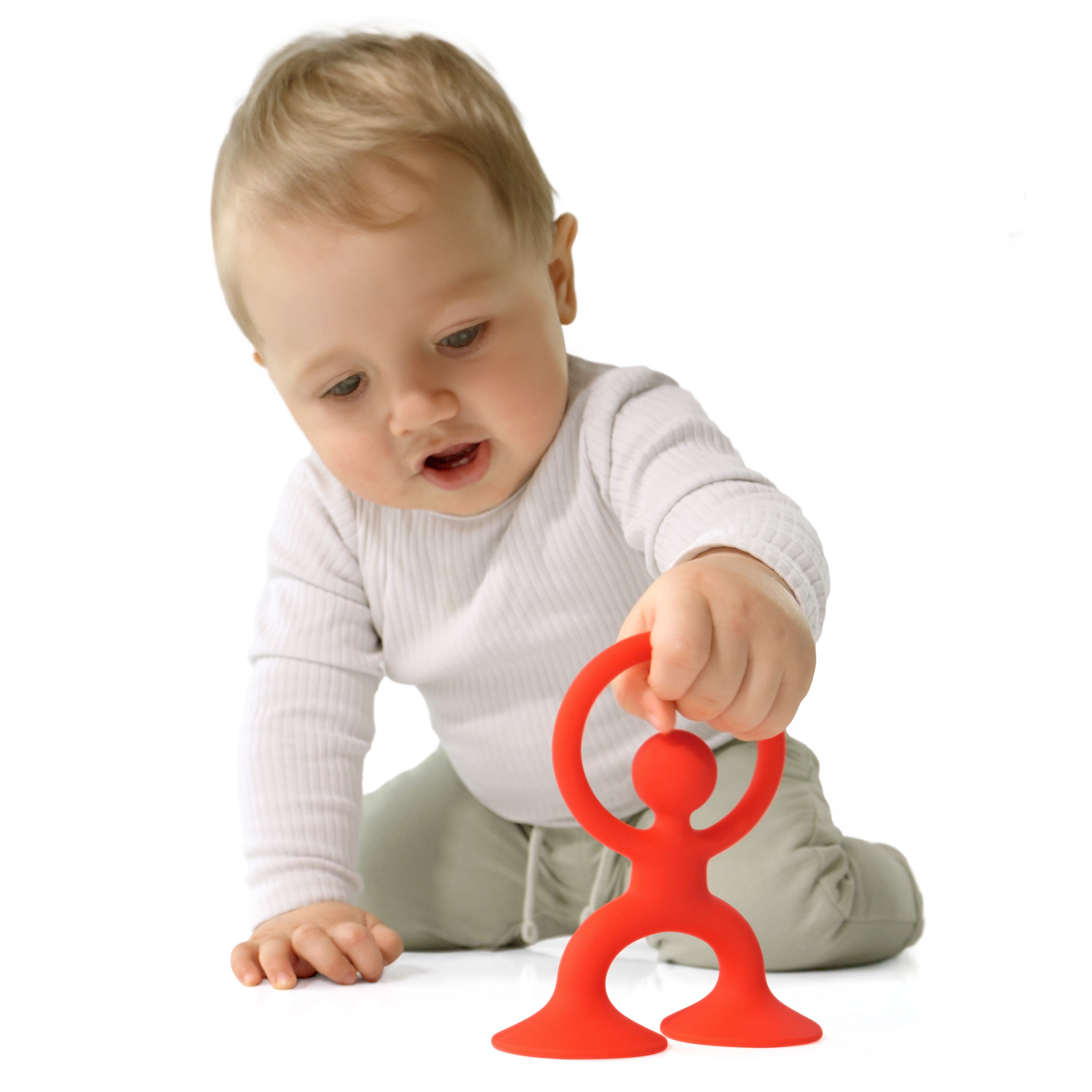 Baby grasping bright red Noogi silicone toy by MOLUK, exploring its friendly shape and suction cup feet during floor play.