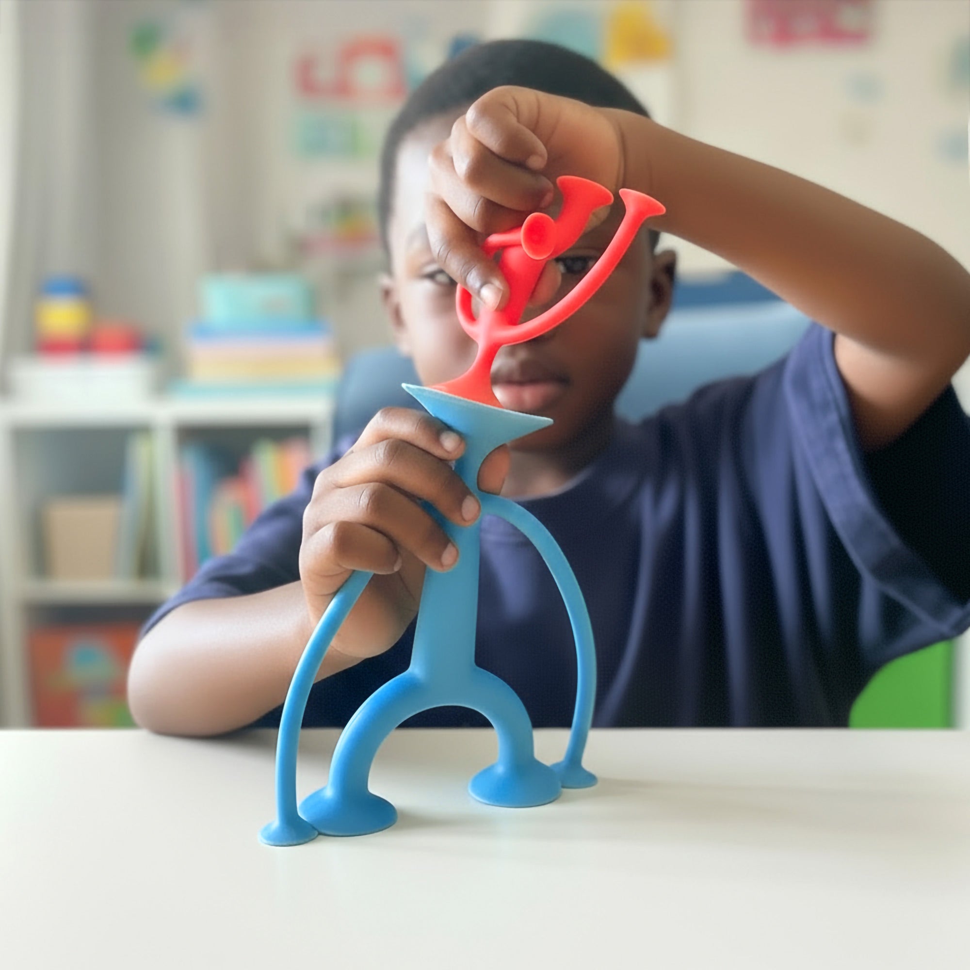 Boy playing with two red and blue Oogi suction cup silicone figures by MOLUK in a classroom.
