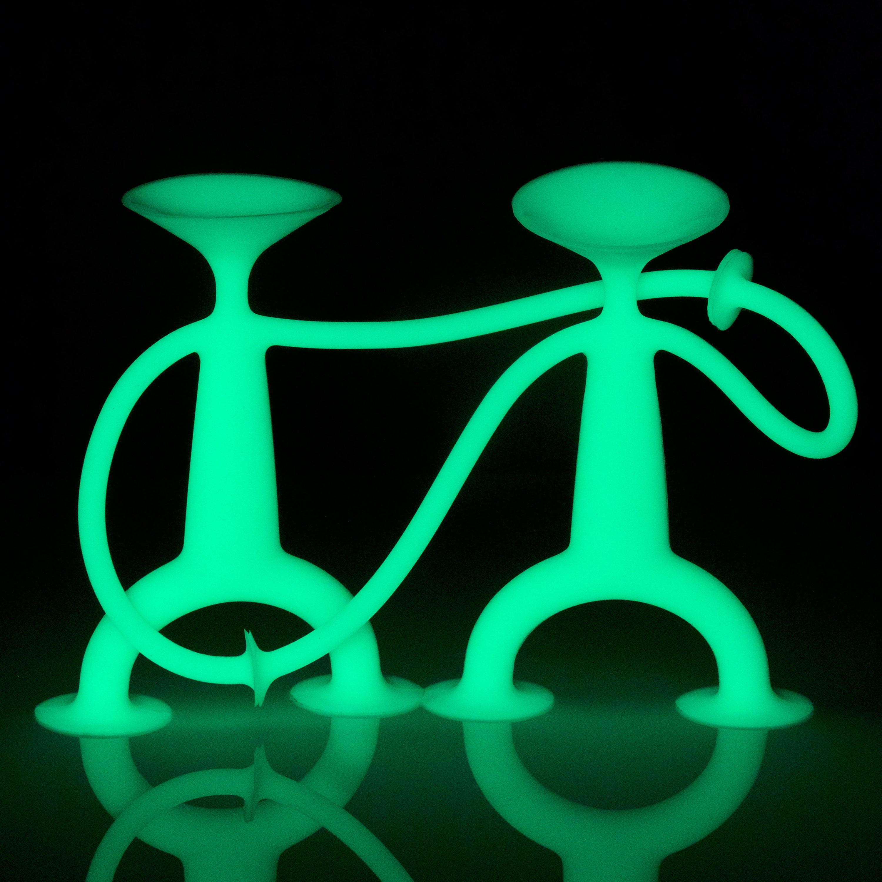 Oogi GLOW silicone suction cup figures by MOLUK glowing in the dark, playfully posing together and holding hands.