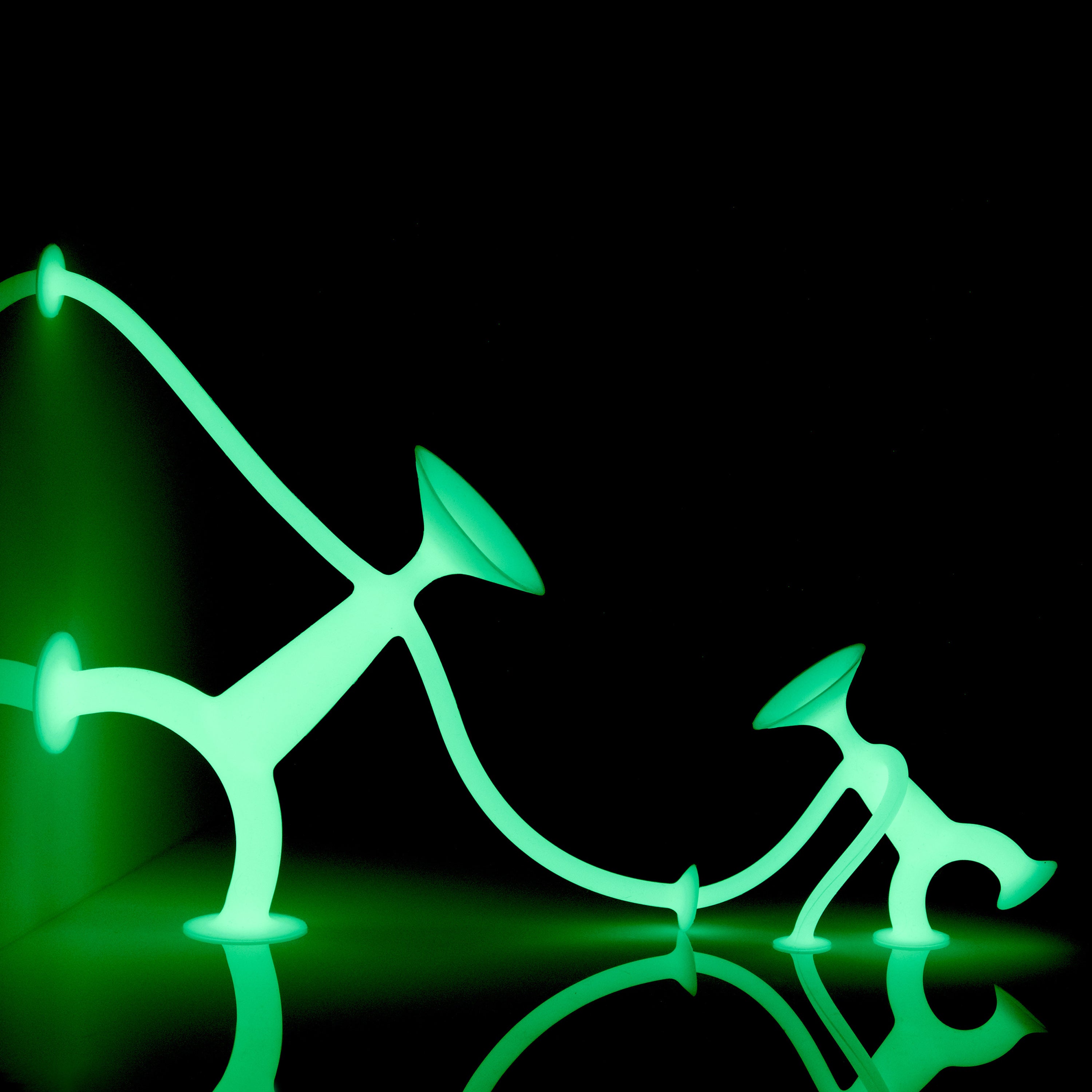 Oogi GLOW and Oogi Junior GLOW silicone suction cup figures by MOLUK glowing in the dark, holding hands.