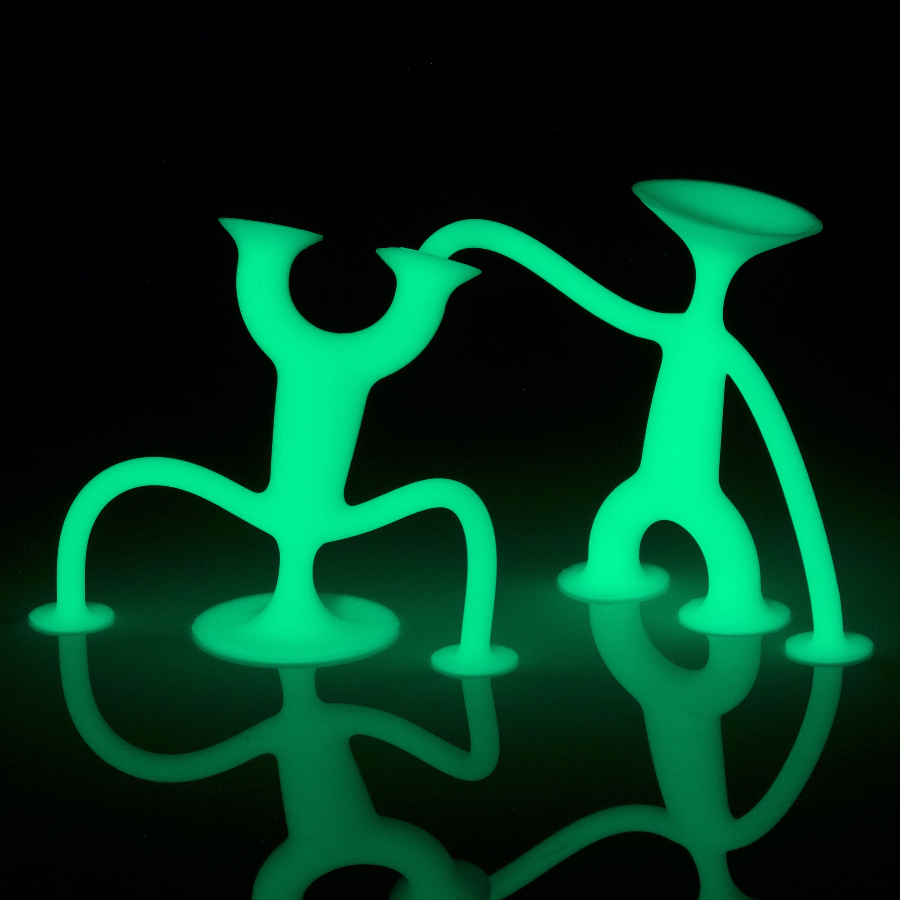 Two Oogi Junior GLOW silicone suction cup figures by MOLUK posing together in the dark.