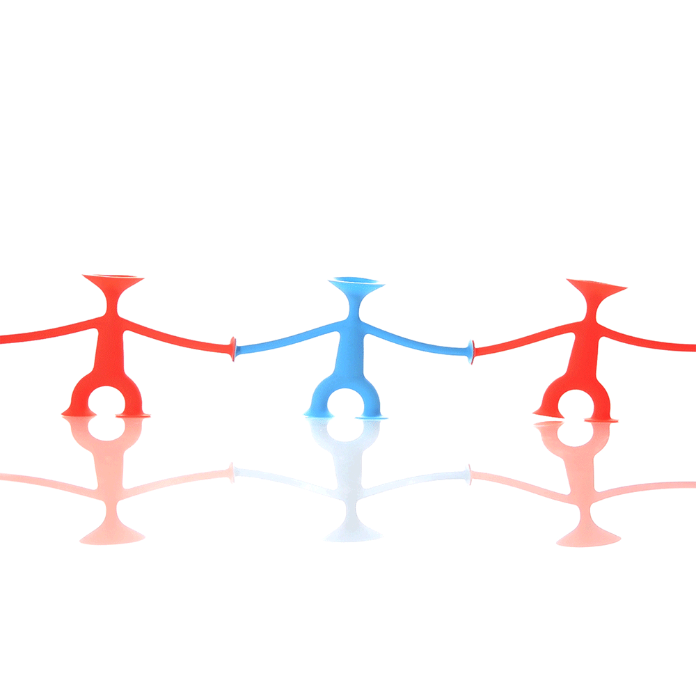 Red and blue Oogi silicone suction cup figures by MOLUK connected hand in hand, forming a playful chain and dancing.