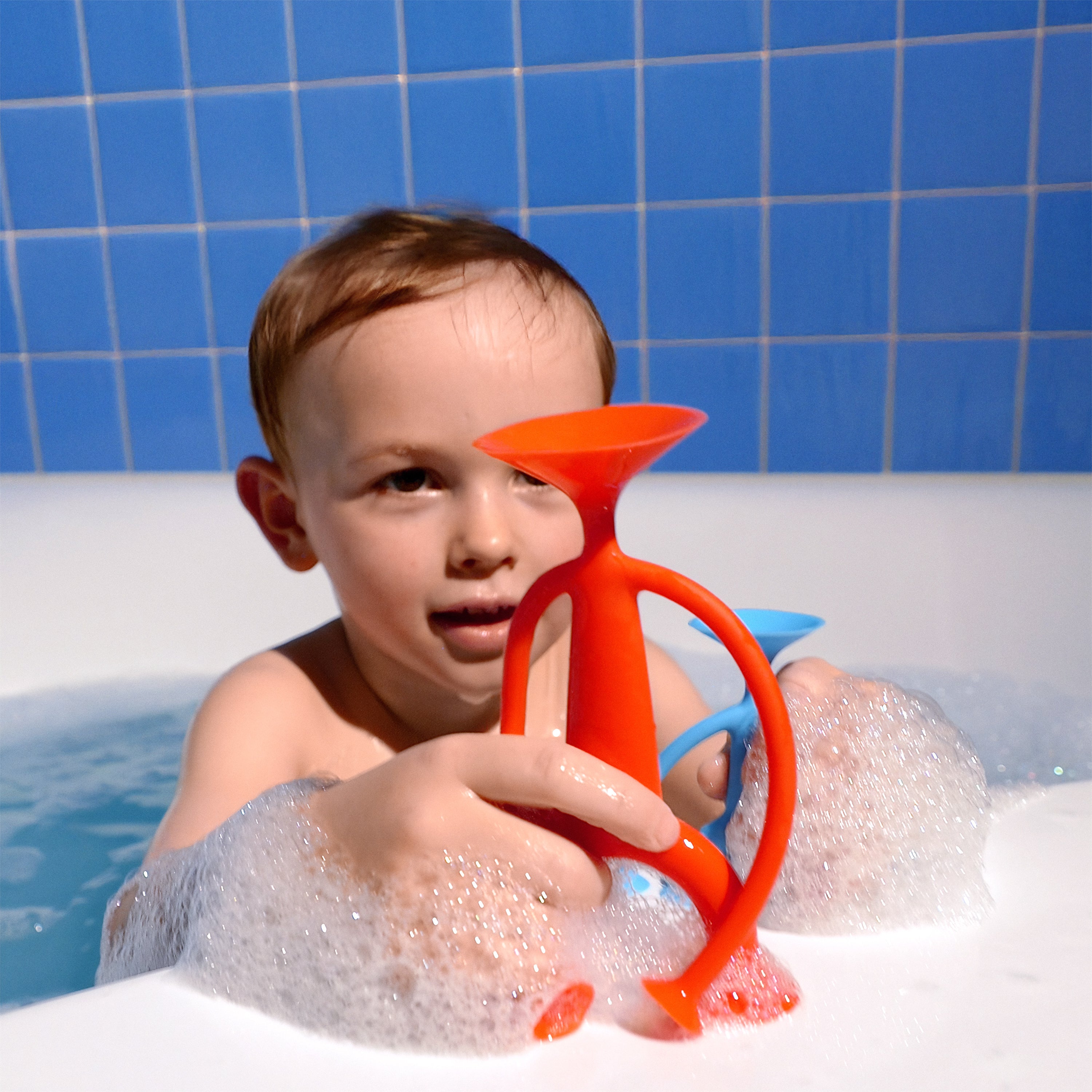 Boy playing with a red and blue Oogi silicone suction cup figure in the bathtub.