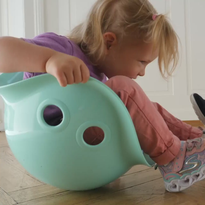 Video of children playing with Bilibo by MOLUK, rocking, spinning, and balancing in colorful shell-shaped seats indoors and outdoors.