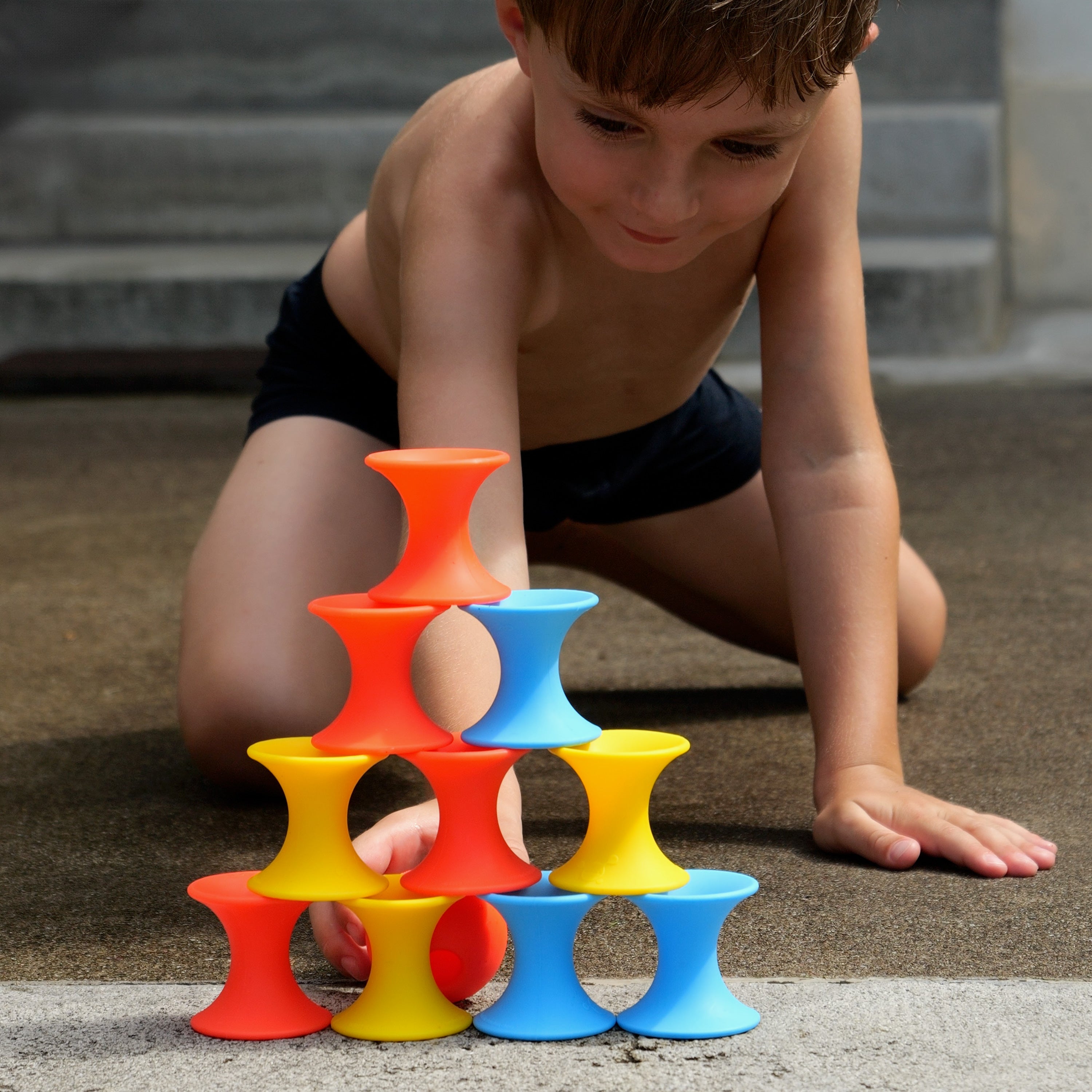 Boy playing outdoors with MOLUK’s Tulu silicone building blocks, stacking red, yellow, and blue pieces into a tall pyramid.