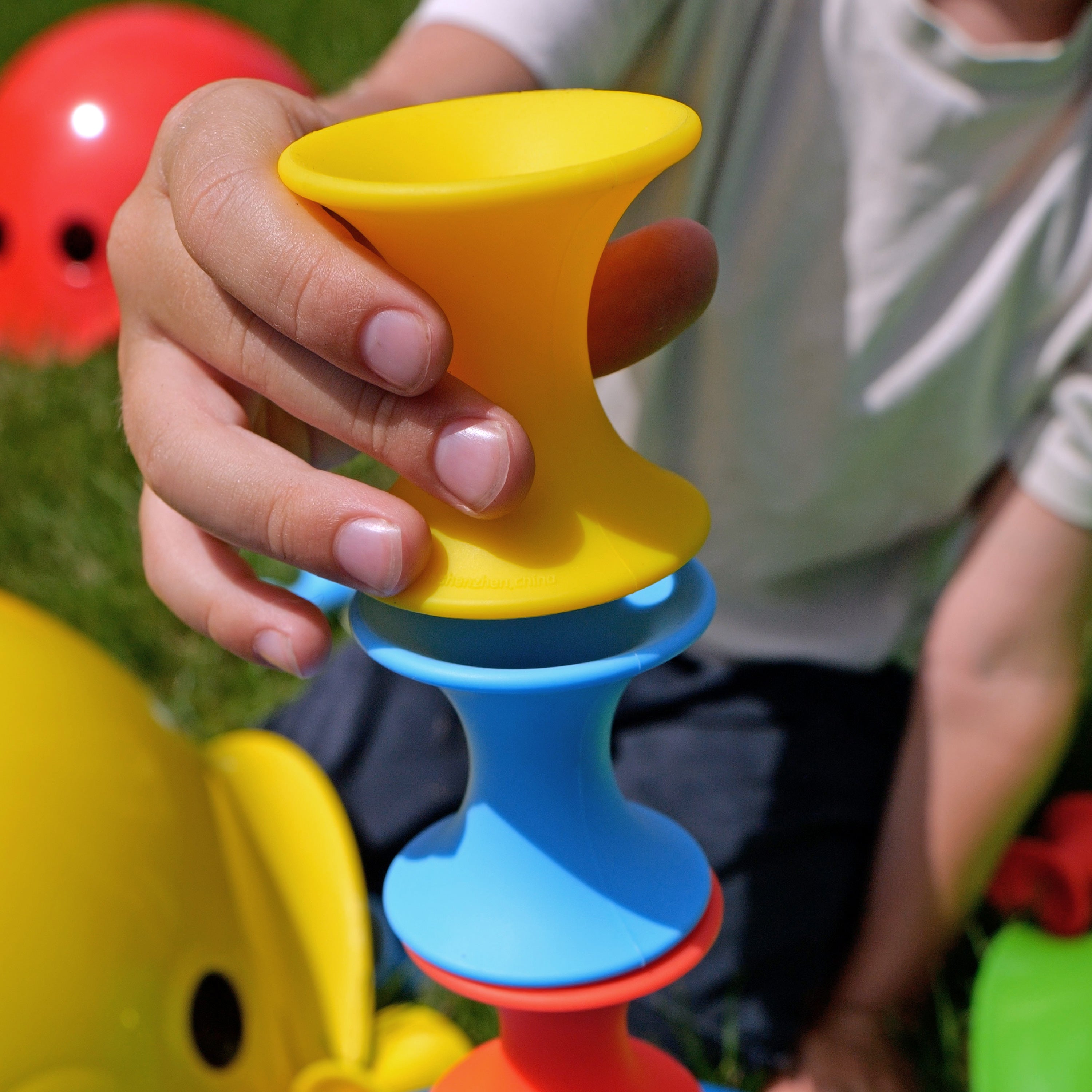 Close-up of a child’s hand stacking MOLUK’s Tulu silicone building blocks in yellow, blue, and red during outdoor play.
