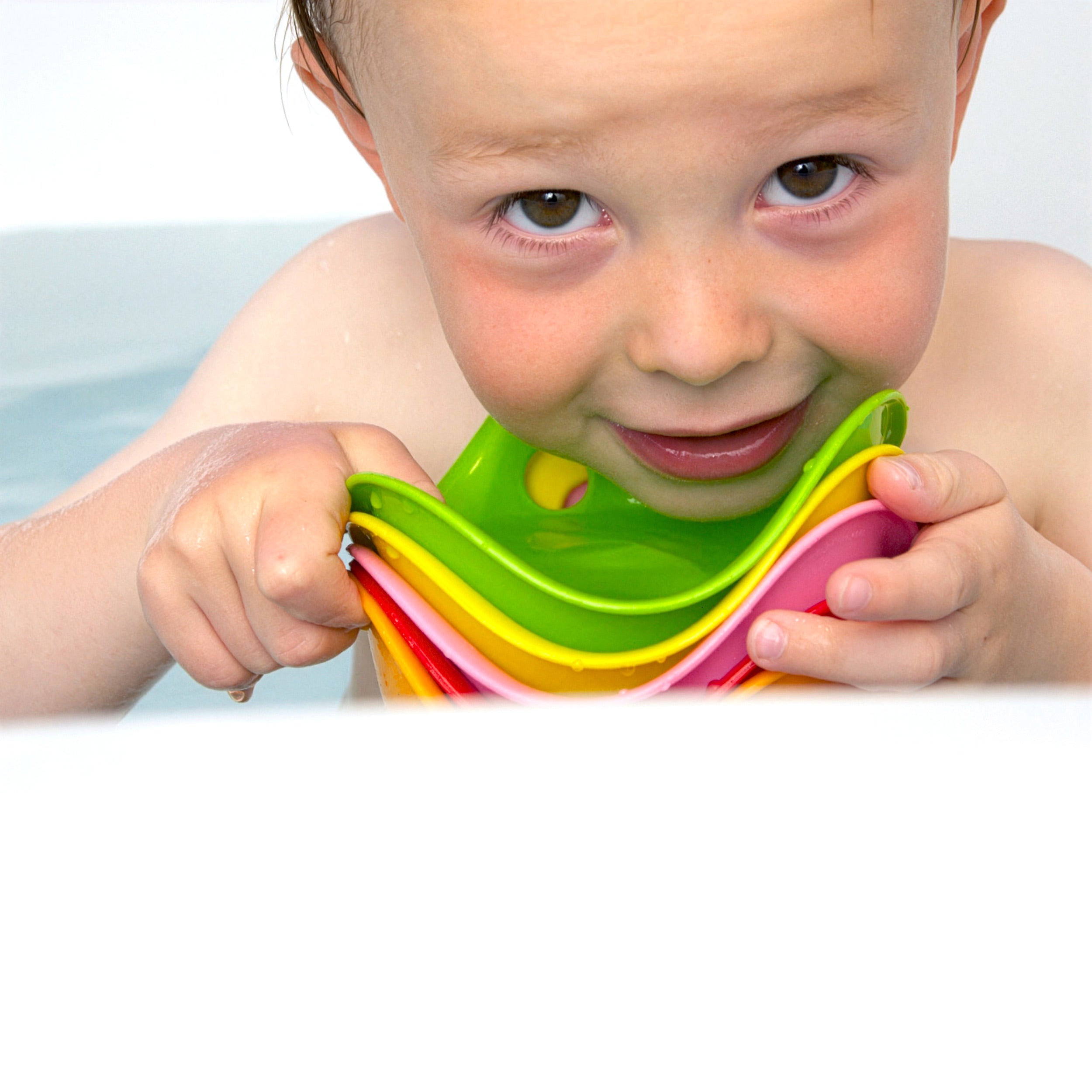 Child in the bathtub holding a colorful set of Bilibo Mini sensory play shells by MOLUK.