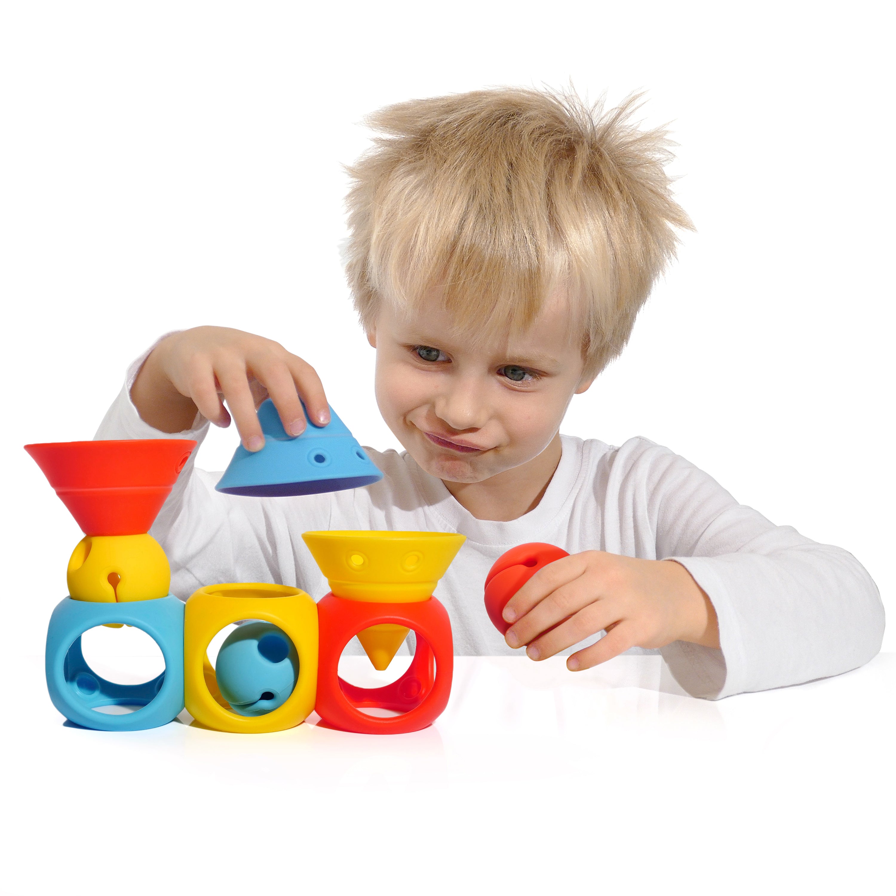 Boy playing with the BUILDING GENIUS set by MOLUK, combining Hix cones, Mox balls, and Oibo blocks in bright primary colors to build a playful toy train.