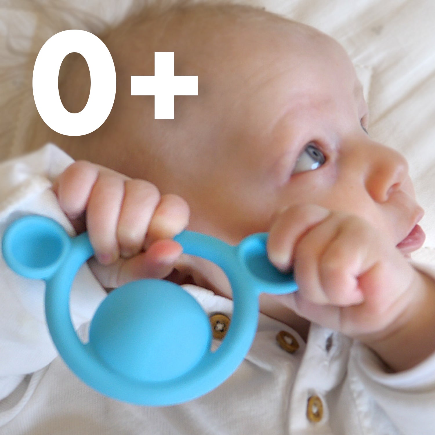 Baby holding a blue Nogi silicone  teething ring by MOLUK with '0+' age recommendation shown.