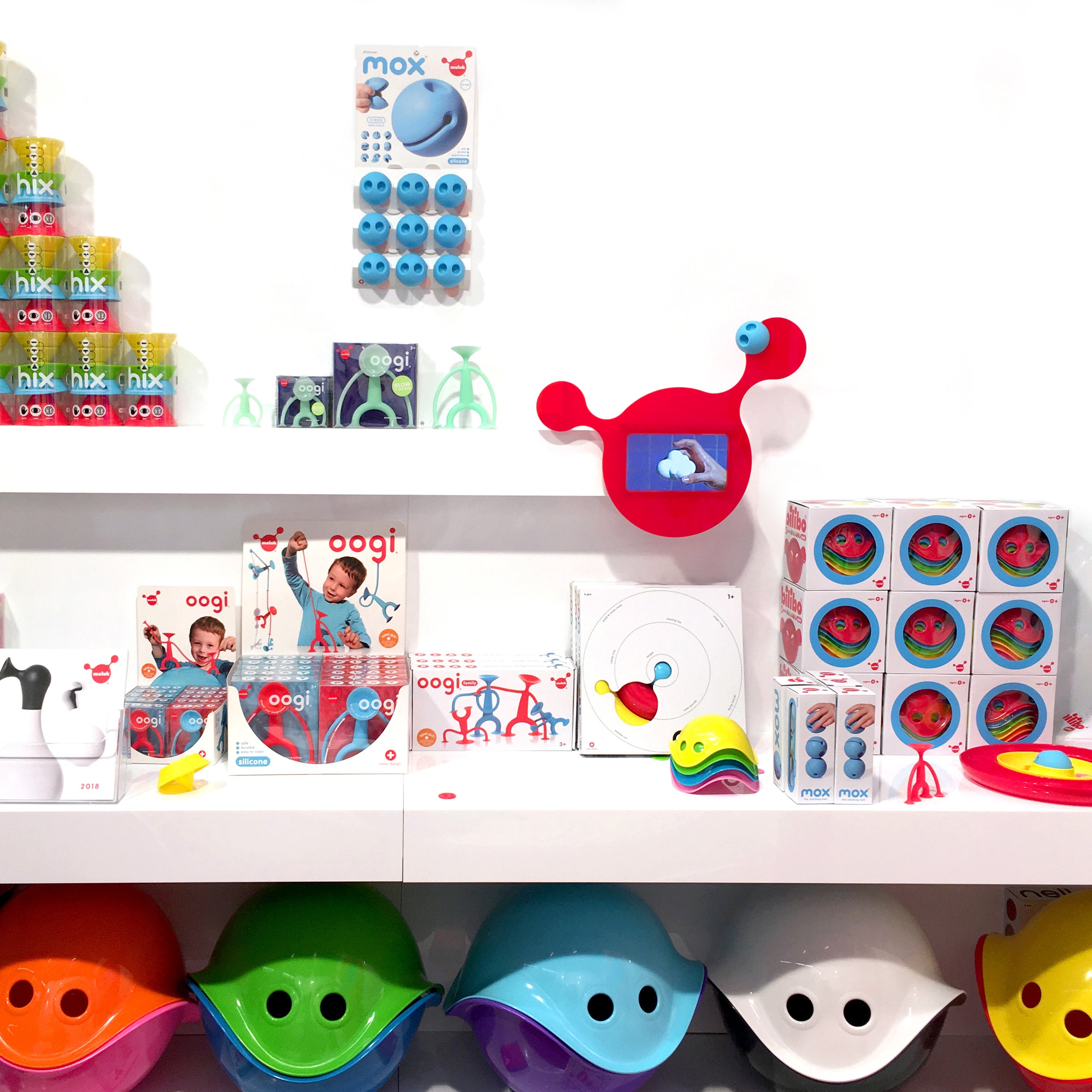 Retail display of MOLUK toys including Oogi, Mox, Hix, and Bilibo in bright colors, with a red wall-mounted MOLUK INSTORE VIDEO screen.