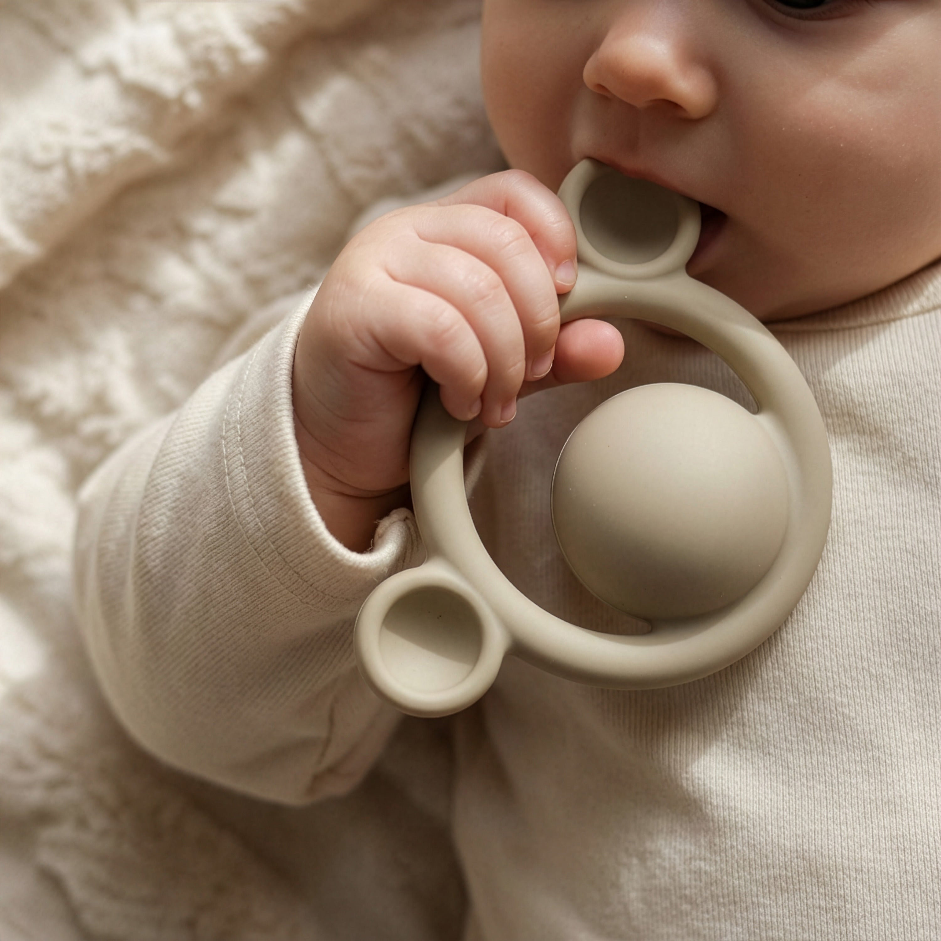 Baby holding and chewing on a beige Nogi teething ring by MOLUK.