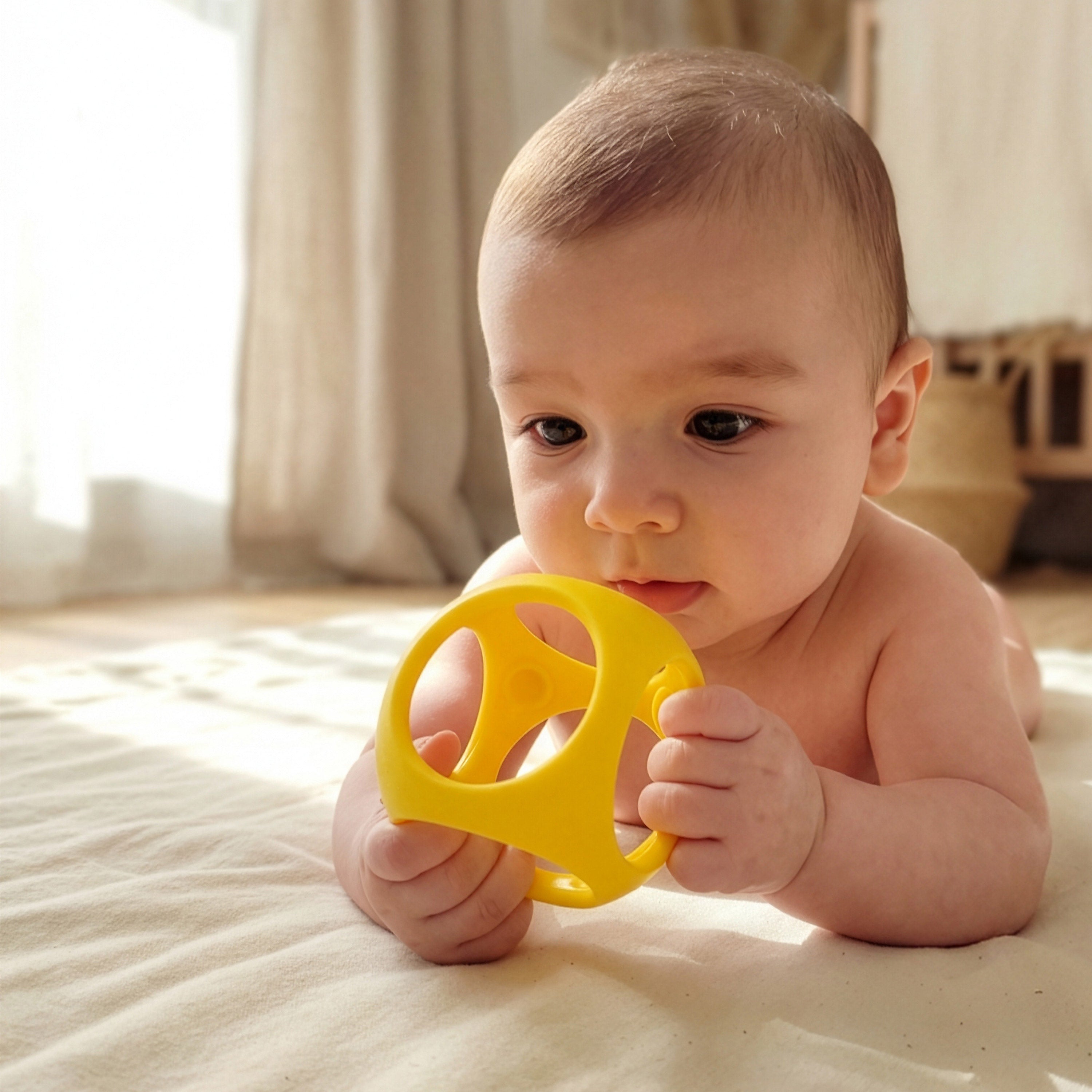 Baby holding a yellow Oibo sensory grasping and teething toy by MOLUK.