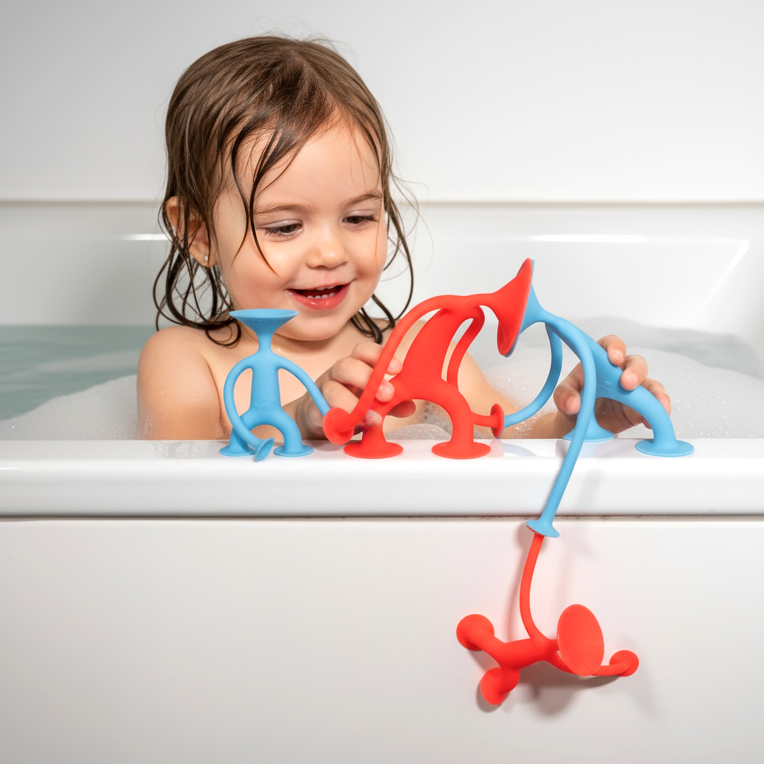 Girl playing with red and blue Oogi silicone suction cup toy figures by MOLUK in the bathtub.