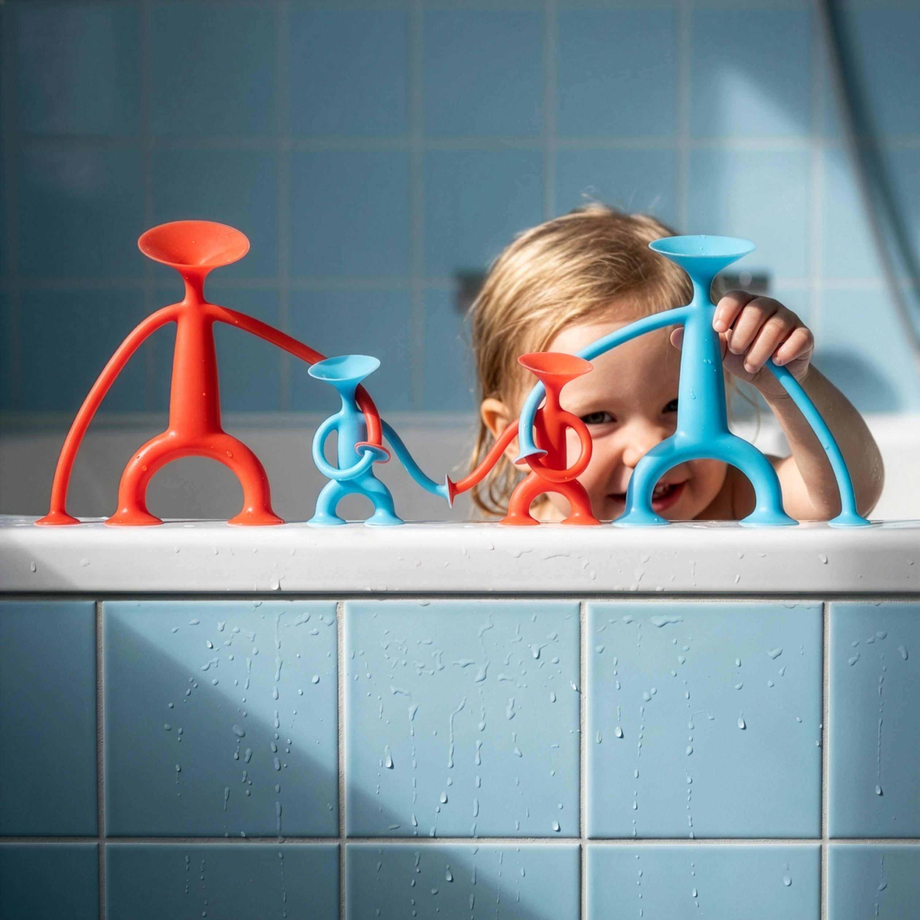 Girl playing with red and blue Oogi silicone suction cup toy figures by MOLUK in the bathtub.