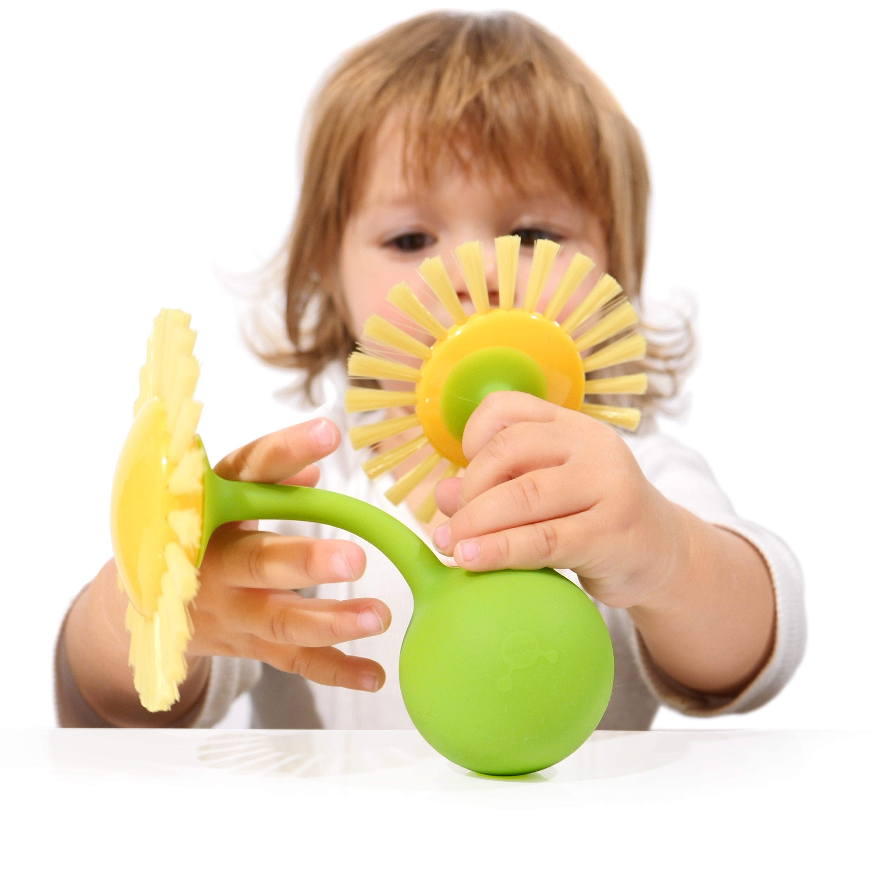 A child playing with two yellow Pluï Brush Sunny sensory toys by MOLUK attached to a green Oogi Bongo to form a flower.